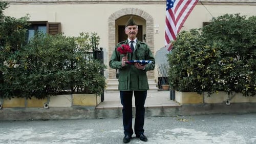 Man Holds Flag and Roses by House