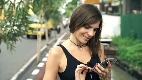 Young Woman Browsing Internet on Smartphone Standing Near Street in City 30s