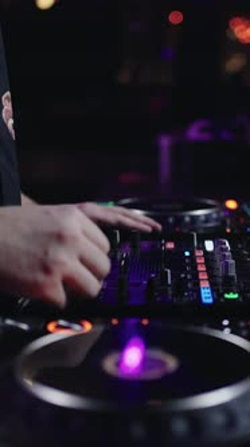 Close Up of DJ Mixing Electronic Music on Illuminated Turntables and Mixer in Dark Nightclub with