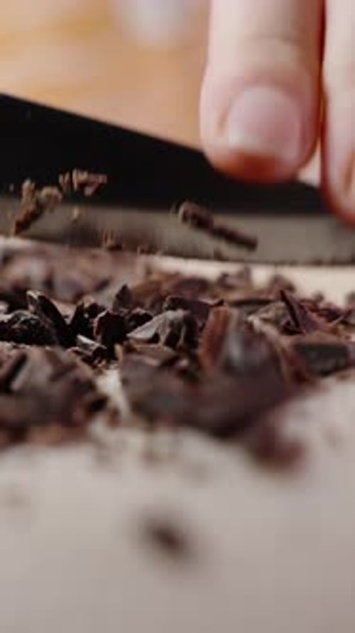 Vertical video. A Woman's Hands Chopping Chocolate With A Knife, Preparing Sweets At Home.