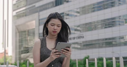 Asian businesswoman standing outdoors in urban business district holding digital tablet with wind