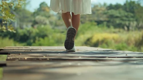 B roll - Rear view of Woman legs wearing sneakers walking on wooden bridge