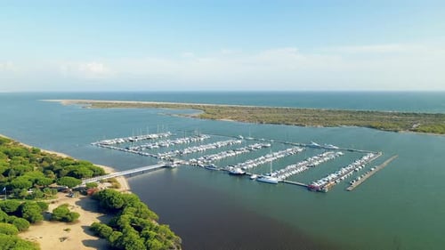 Aerial pull back from Puerto Marina El Rompido docks with many yachts, sailboats, watercraft, and pi