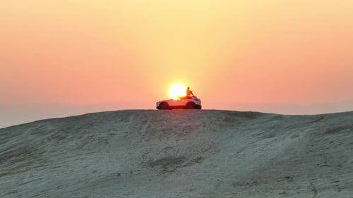 
Man sits on a desert hill overlooking a sunrise in on top of a car