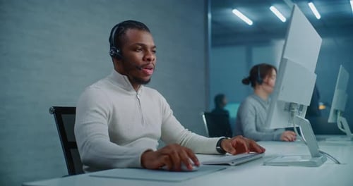 African American Hotline Operator Talks on Headset with Customer Works on Computer