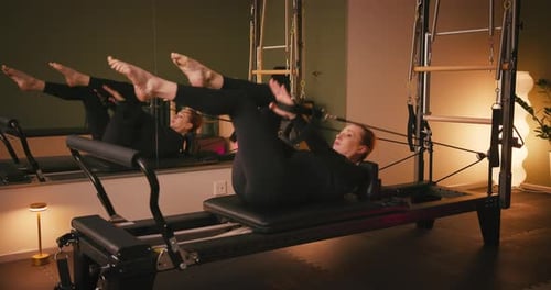 Woman Exercising on Pilates Reformer Machine in Gym