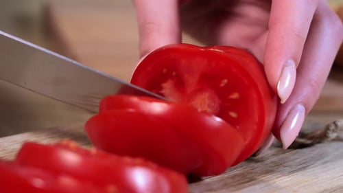 Woman Slicing Red Tomato with Knife on Board