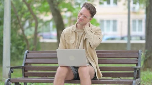 Young Man Massaging Neck While Using Laptop in Park