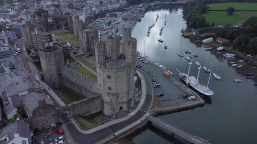 Ancient Caernarfon castle Welsh harbour town aerial view medieval waterfront landmark slow left over