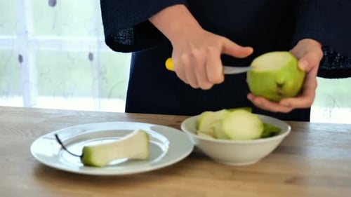Green pears.woman cuts a ripe pear with a knife into a plate on a wooden table