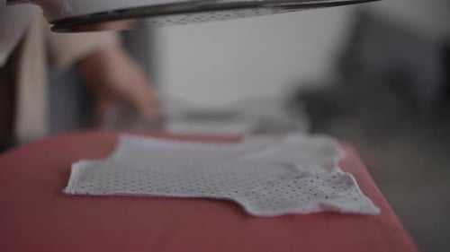 Slow Motion Closeup An Unrecognizable Woman Steams and Irons a Baby Tshirt with a Steam Iron on an