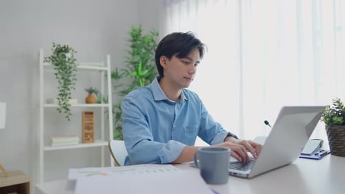 Man Works on Laptop and Drinks Coffee at Desk