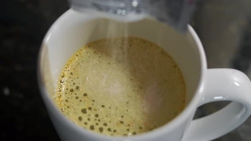 Close up shot of orange juice powder been poured into water in a white cup and foam arising in the c