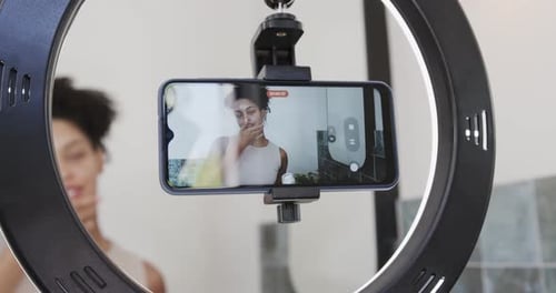 African American woman recording after red dot on phone in bathroom ring light demoing skincare