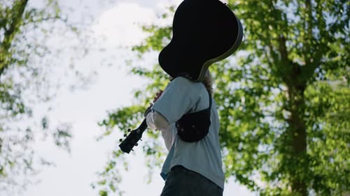 Young Man Carrying Guitar in a Green Park