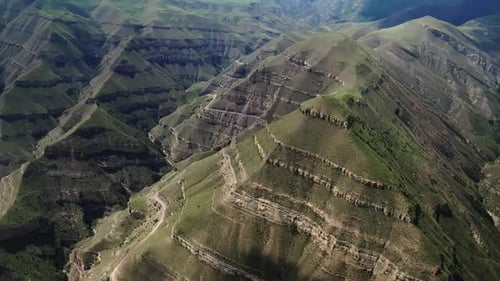 Aerial View of a Mountain Range with Lush Slopes Terraced Fields and Snaking Roads Under Sunlight