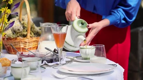 Close up shot of woman's hands serving tea in a cup on a breakfast table