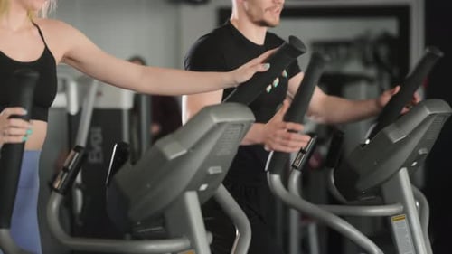 A Man and a Girl are Working Out on an Elliptical Trainer