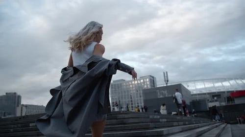 Active woman walking stairs energetically in evening city clouds back view