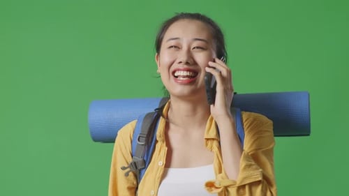 Asian Female Hiker Talking On Smartphone And Looking Around While Walking On Green Screen