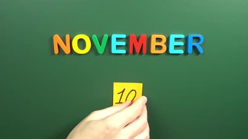 Hand sticking a sticker 10 November calendar day on school board. 10 date of November. Tenth day