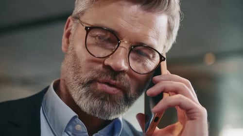 Closeup View of Goodlooking Grayhaired Middleaged Caucasian Talking on Smartphone While Drinking