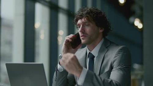 Business Executive Sitting with Laptop and Having Phone Conversation in Cafe