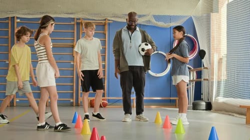 Black Man as Coach Explaining Soccer Drills to Children in Gym