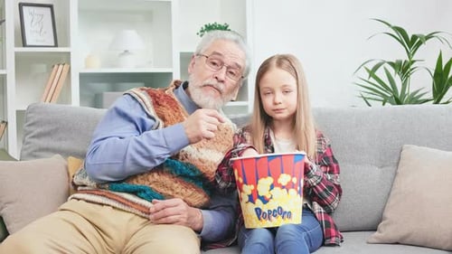 Child and Senior Sharing Popcorn on Couch