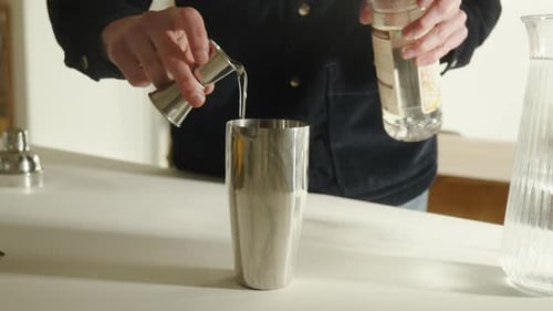 Hobby bartender pouring simple syrup from jigger into cocktail shaker in the kitchen at home. Close