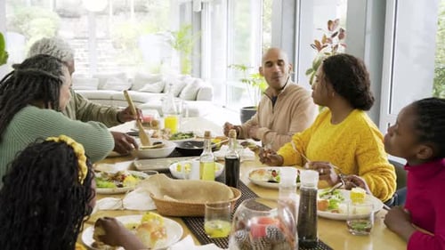 After grandma passing salad bowl, African American man raising fork, joining chat at dining table