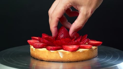 The pastry chef is placing the last strawberry on top of a custard cream filled tart