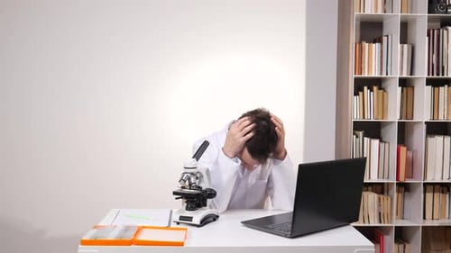 Young Male Scientist Wearing a Lab Coat Feeling Stressed and Frustrated with Hands Clutching His