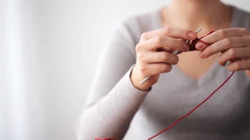 Woman crocheting red yarn with a silver hook
