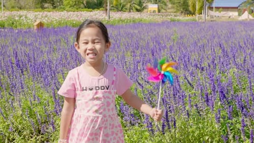 Portrait of a Smiling Girl in a Flower Garden Holding a Toy Pinwheel Spring Brings Joy and the