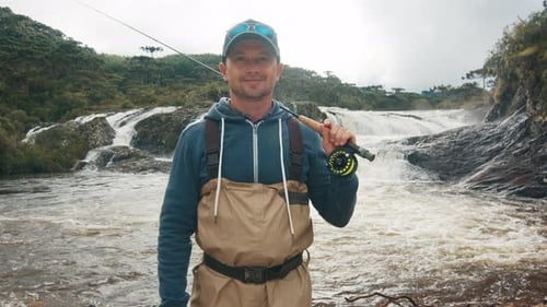 Man Stands in River Holding Fishing Rod