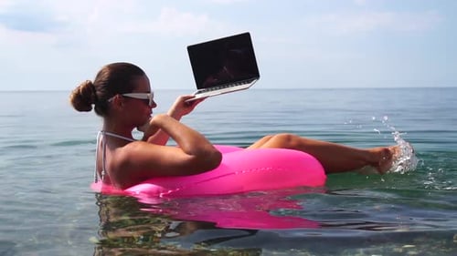Woman Freelancer Works on Laptop Swimming in Sea on Pink Inflatable Ring Happy Tourist in Sunglasses