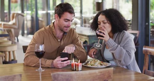 Smiling mixed race couple using a smartphone together while having lunch at a restaurant