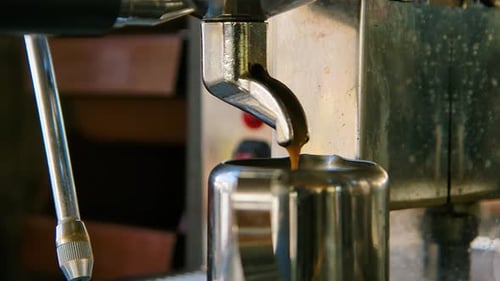 Closeup orbit of coffee dripping out into metal tea cup in slow motion