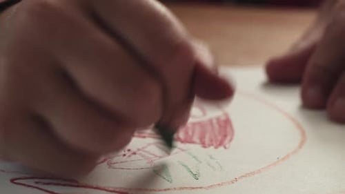 Ein Kind fügt einer Zeichnung eines Hauses mit einem Buntstift grünes Gras hinzu, während die Kamera nach rechts zeigt.