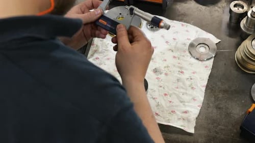 Worker measuring metal part with micrometer in workshop, close-up, industrial setting