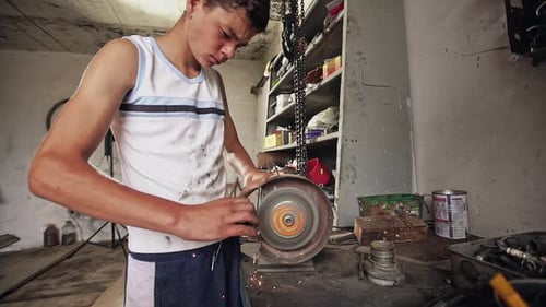 Teenager Using Grindstone in Workshop