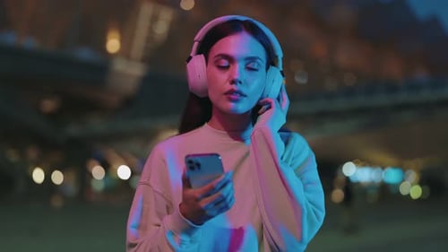 Woman With Headphones Using Mobile Phone at Night