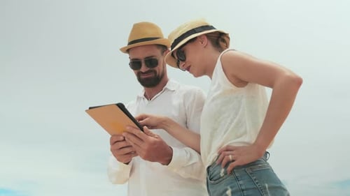 Couple On Beach Looking at Tablet Together
