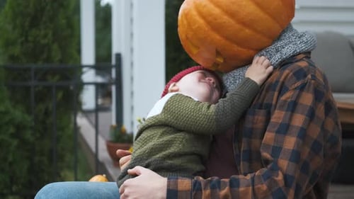 little boy playing with father with halloween pumpkin head on terrace