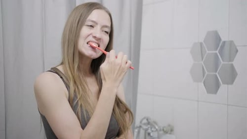 Woman Brushing Teeth in Bathroom with Tooth Pain