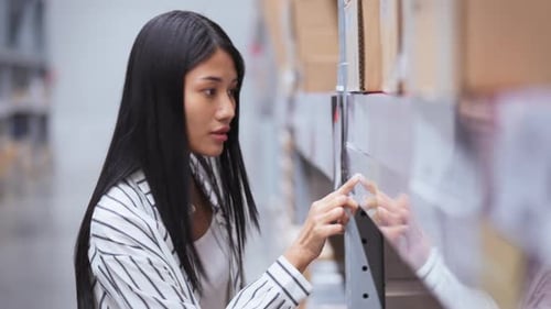 Woman Browsing Boxes in Large Warehouse Aisle