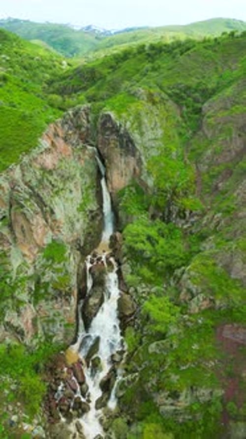 Ein atemberaubender Wasserfall stürzt felsige Klippen hinunter, umgeben von üppigem Grün und bergigem Gelände