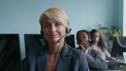Jeune opératrice blonde à succès avec casque regardant la caméra