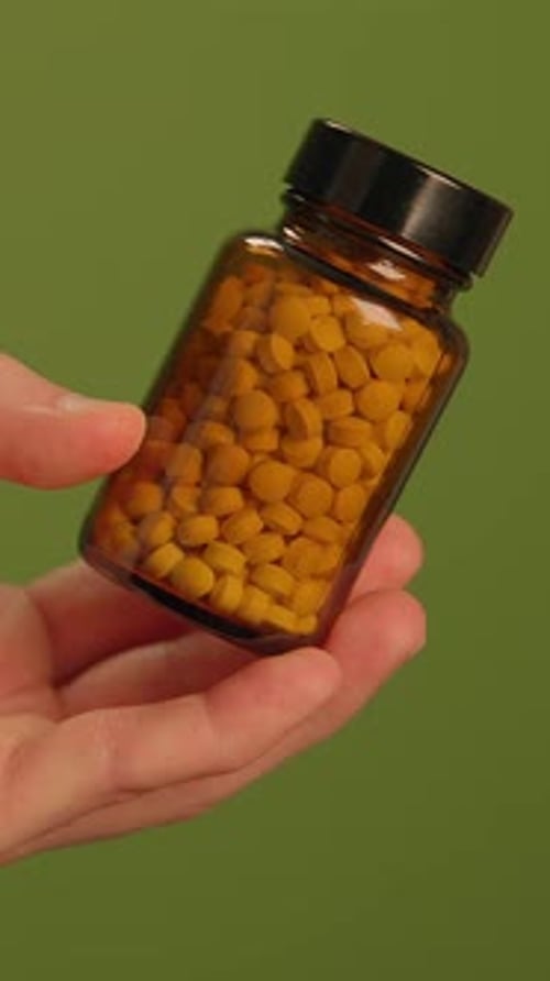 Hand Holding Bottle of Yellow Pills